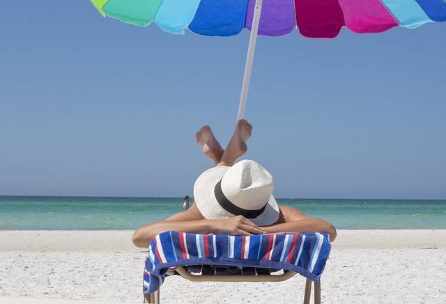 picture of a person laying on the beach under an umbrella with water in the background